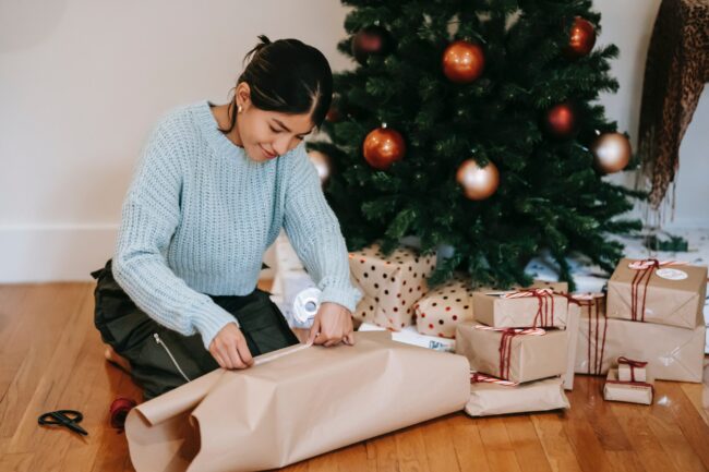 femme qui emballe des cadeaux de Noël à côté du sapin