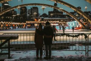 Couple face à une patinoire de Noël illuminée de guirlandes et décorée d'étoiles.