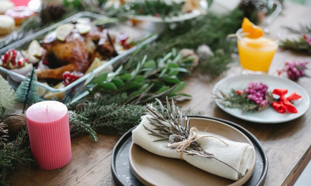 Table de Noël décorée avec des bougies et branches de sapin. Un plat de dinde est au centre de la table.